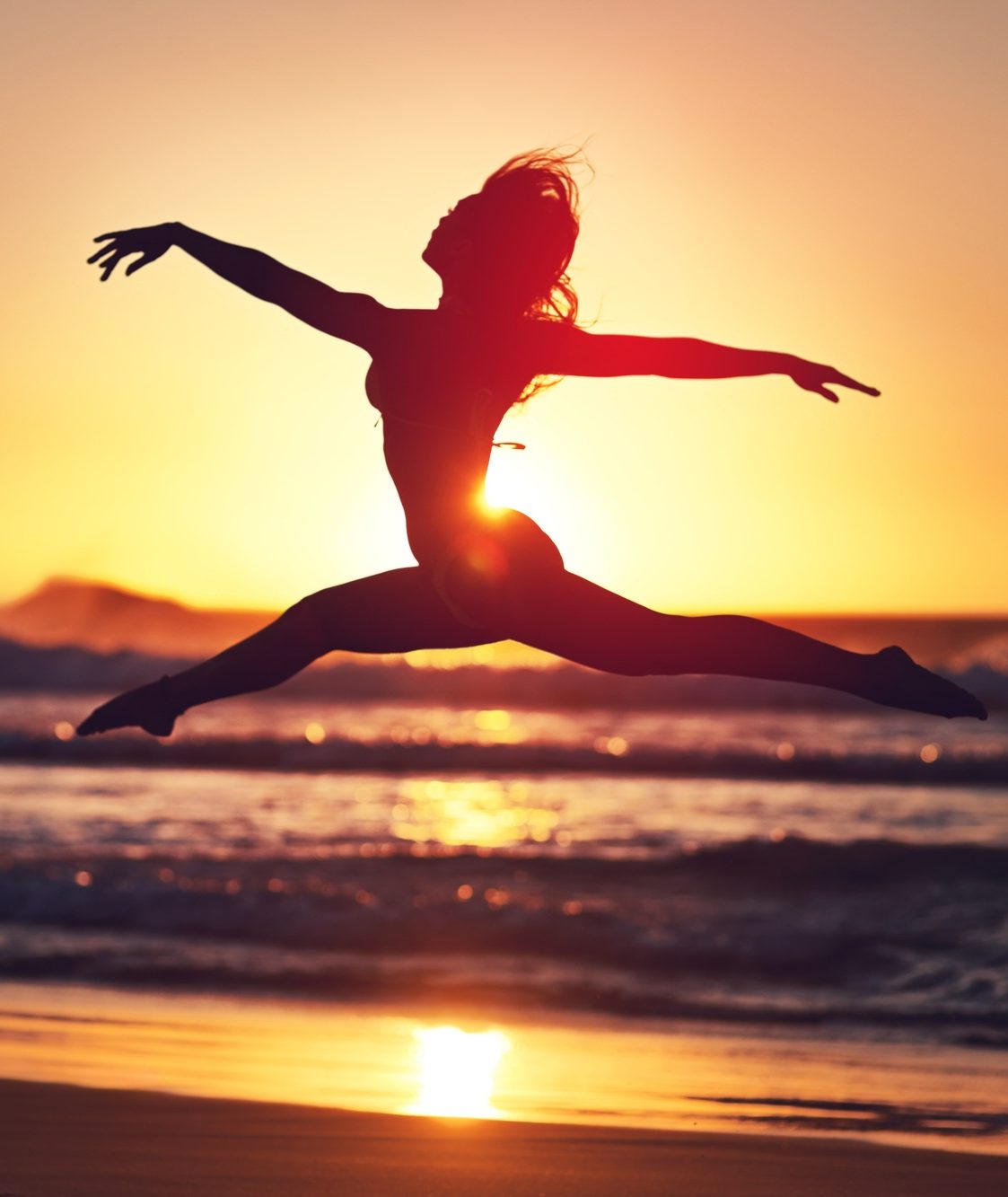 Take a risk. Silhouette of an energetic woman jumping on the beach at sunset.