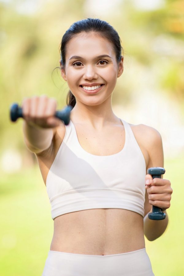 Enthusiastic young woman with a bright smile, working out with dumbbells outdoors